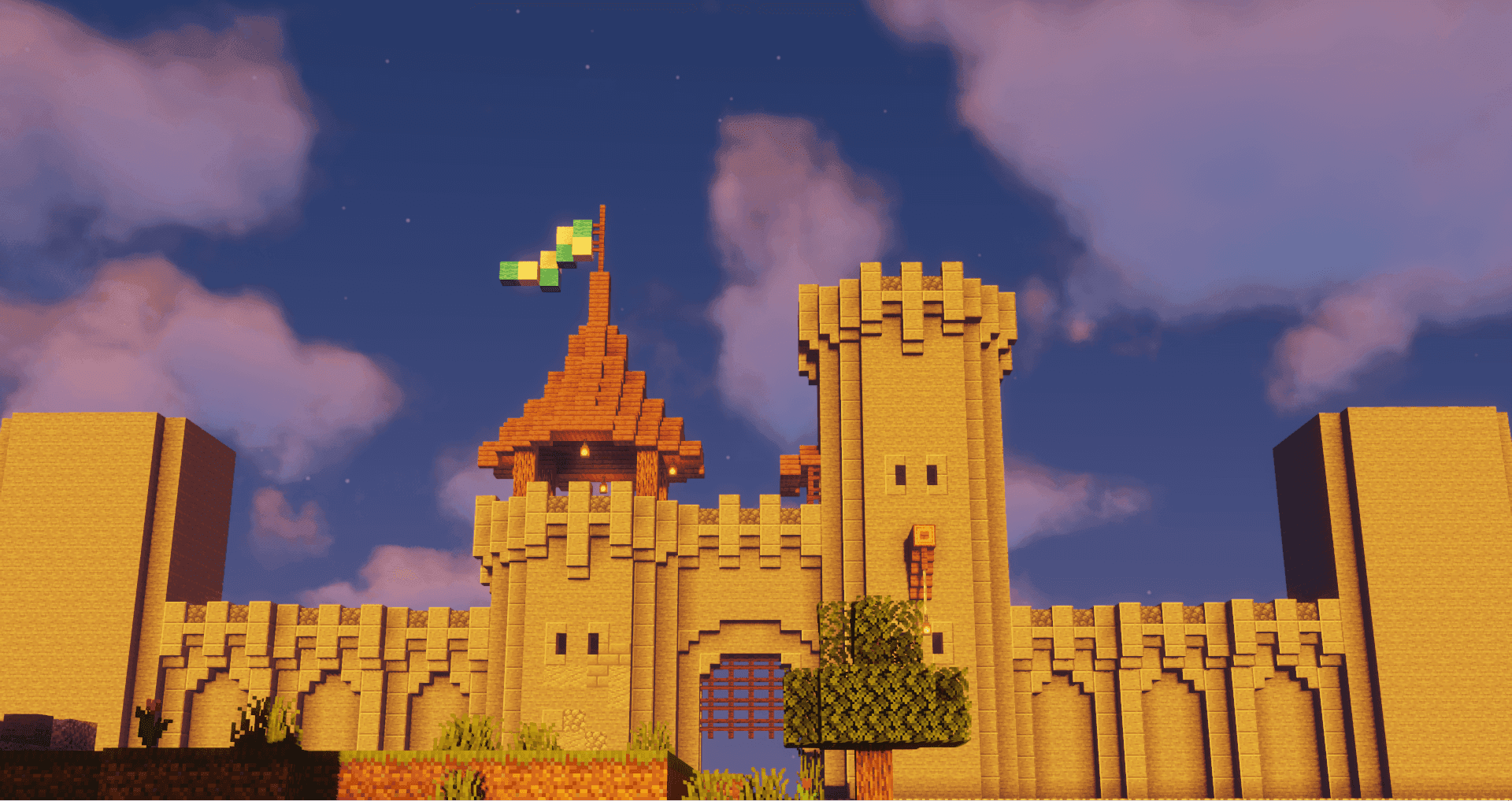 A castle wall and gatehouse with a tall square tower and a small striped flag at dusk.