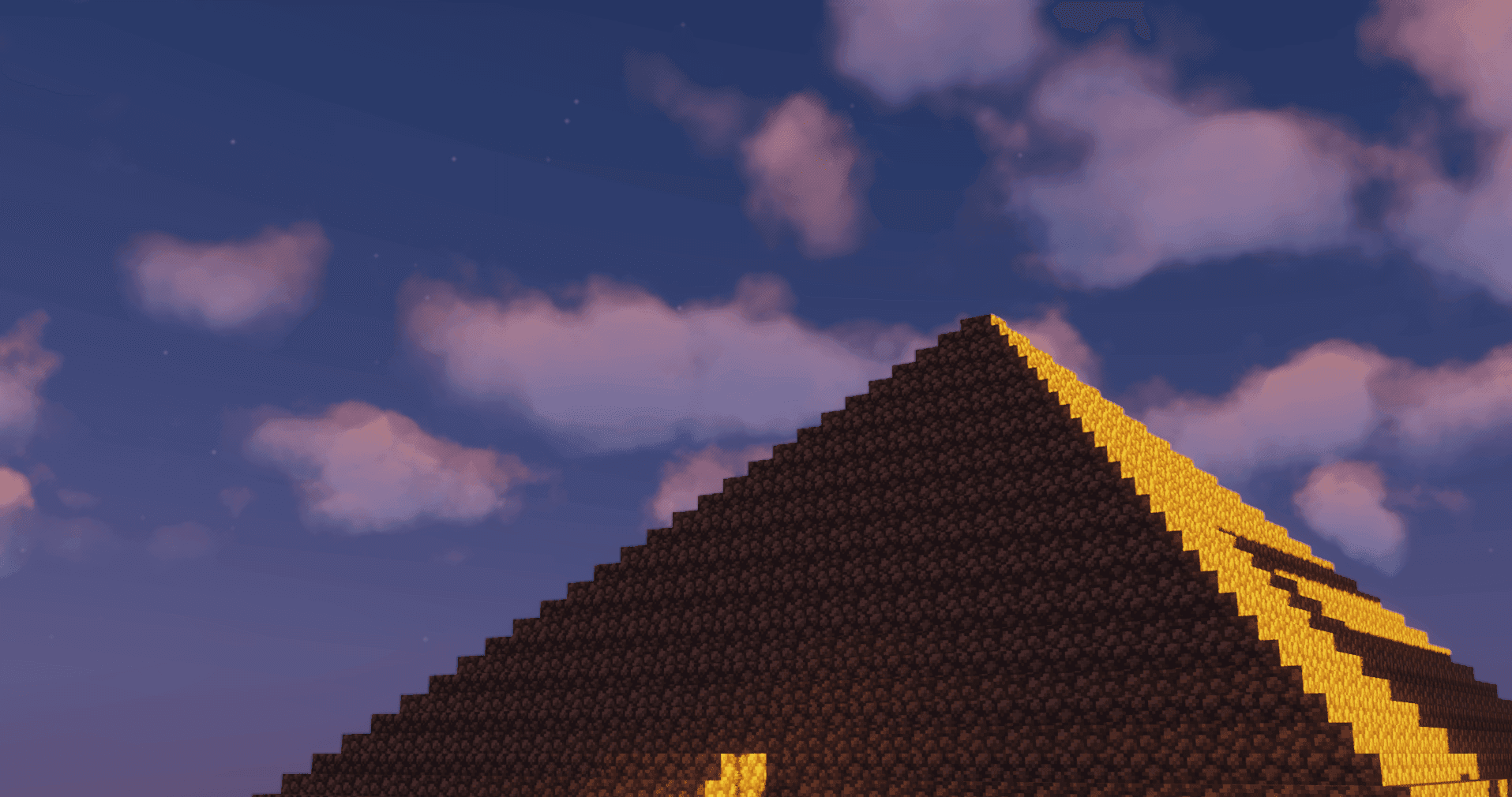 The steep roofline of a large dark stone building glowing under a pink evening sky.