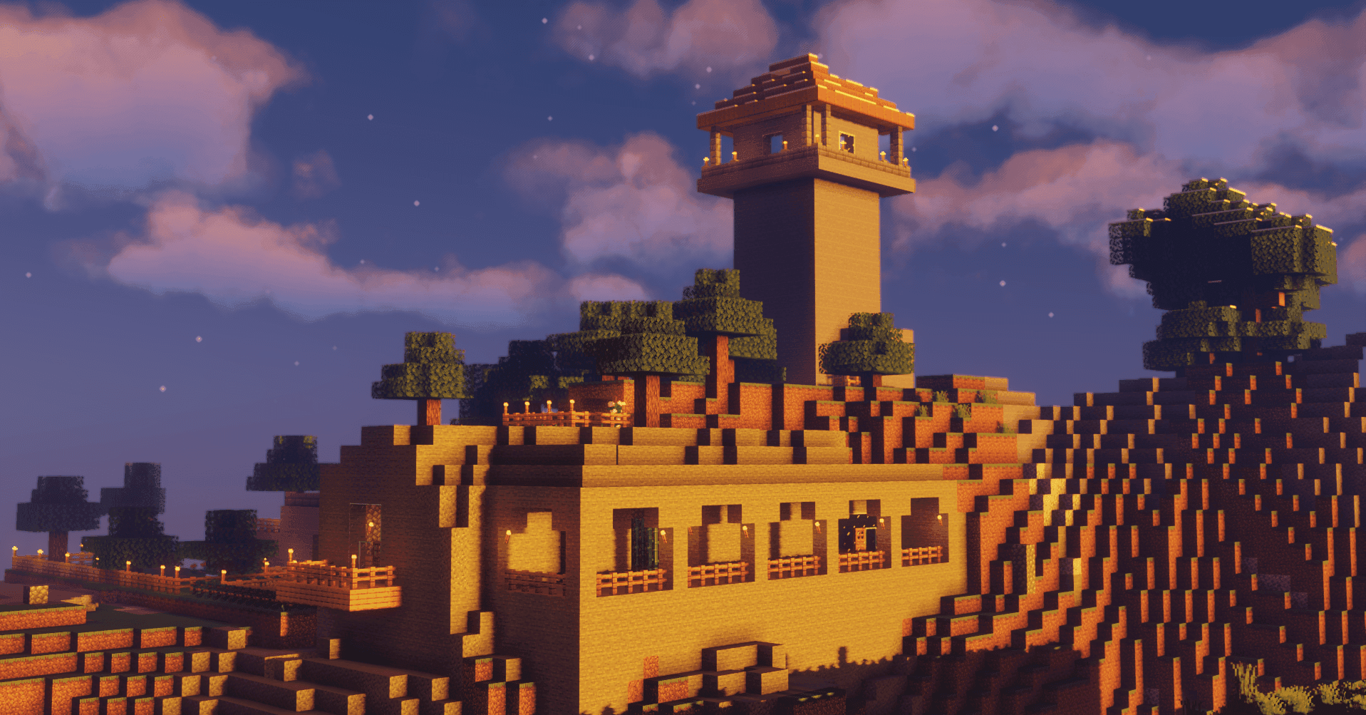 A torch-lit hilltop base with a tall watchtower above terraced buildings at dusk.